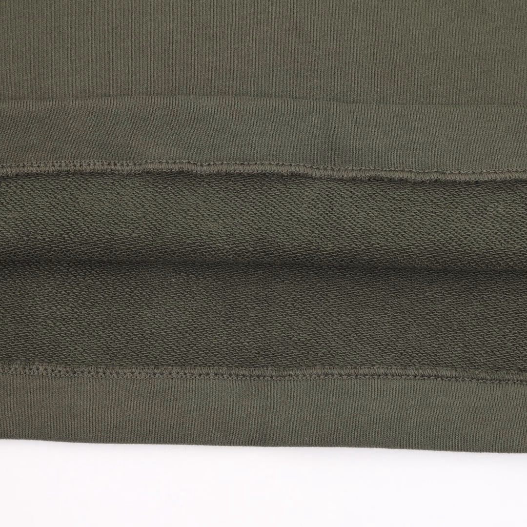 GUC letter embroidered shortsSingle-sided fish scale fabric woven with cotton as the base, the front is a smooth knitted surface, and the skin-touch surface is formed into a three-dimensional terry loop through the floating thread knitting technology of the knitting machine, which increases the fluffiness and delicate touch. The terry loop structure absorbs a lot of water and evaporates quickly, and it is not easy to loosen and deform after multiple washings. The same color fabric is cut into the brand letter pattern by laser, and the patch is temporarily fixed on the base fabric through hot melt adhesive film to ensure that the position is completely consistent with the design drawing. The same color thread is embroidered along the inner contour of the patch through a flat embroidery machine to form an invisible fixing layer to prevent the patch from shifting. By actively intervening in the shrinkage potential of cotton fibers, the fabric has achieved a leap from changeable to stable, improving dimensional stability, and is not easy to deform and wrinkle.
