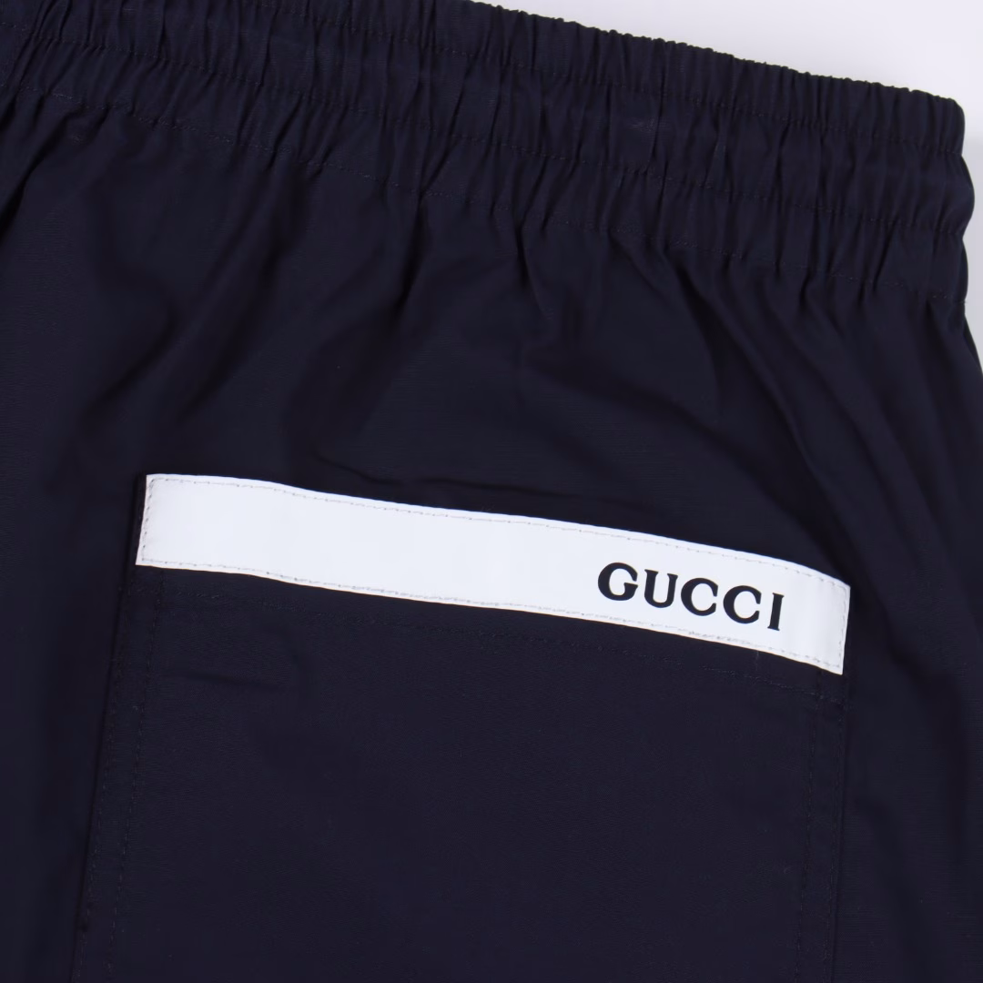 GUC back white label poplin shortsThe cotton fiber is selected to form a plain weave method with twice as many warps as wefts, forming a fine and uniform diamond-shaped particle texture on the surface, smooth to the touch and slightly shiny cotton poplin fabric. Pure cotton material is moisture-absorbent and breathable, and not easy to get stuffy. The high-density structure enhances its wear resistance while also having good wrinkle resistance. The rubber strip is engraved with a high-precision laser beam, and the edge accuracy is ensured to be ±0.1 mm through a dynamic focusing system, thus forming a high-precision letter LOGO. Then use a heat press (temperature controlled at around 150°, pressure 5kg/CM²) to bond the rubber strip to the fabric, and finally carve the same color line at the edge, firmly decorated on the back patch pocket, the elastic waist has built-in elastic silicone tendons to fit different waist shapes, and the outside is equipped with an adjustable drawstring buckle, fixed with a customized buckle head, and the tightness can be fine-tuned with one hand, taking into account both practicality and aesthetics. One-to-one customized drawstring buckle, letter LOGO rubber strip