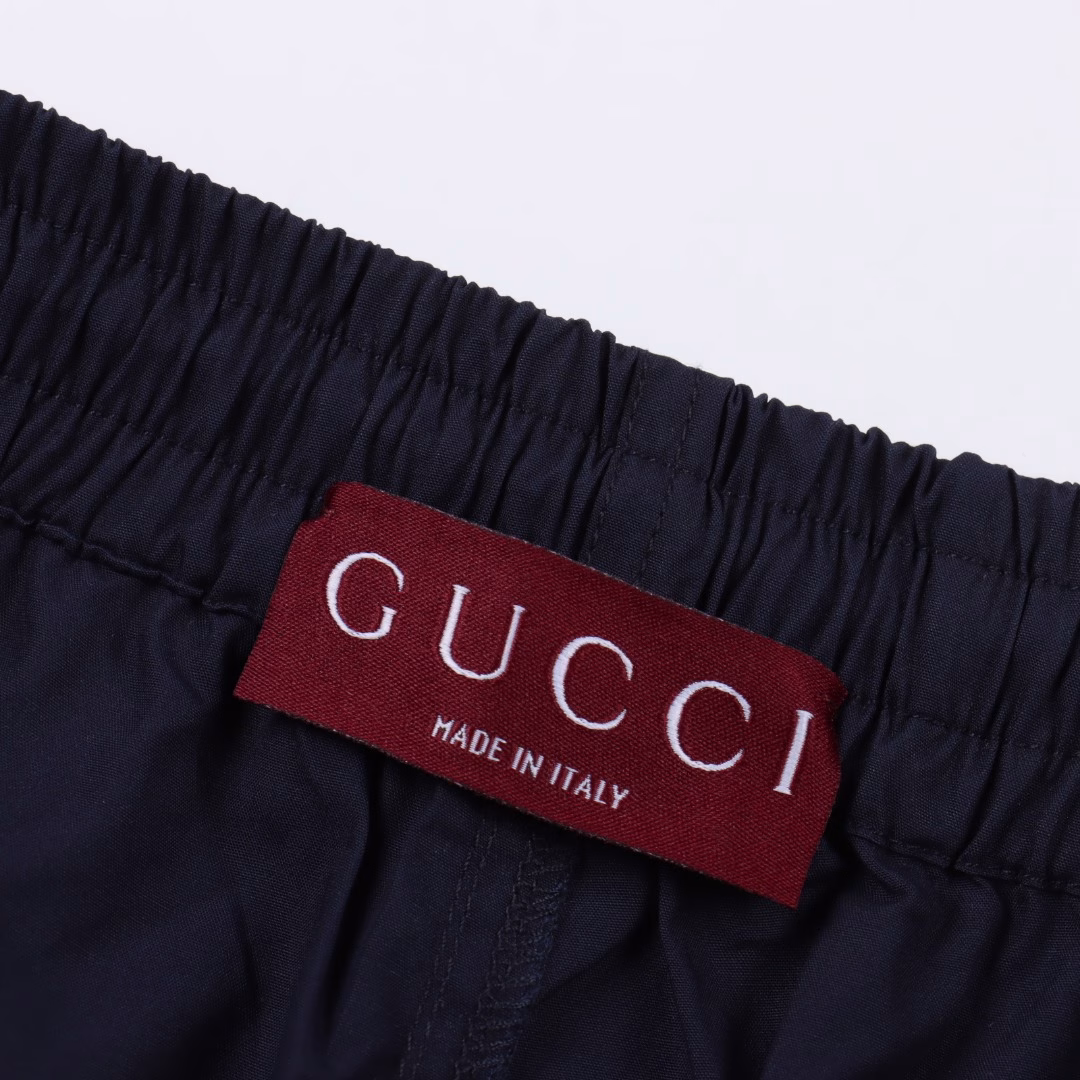 GUC back white label poplin shortsThe cotton fiber is selected to form a plain weave method with twice as many warps as wefts, forming a fine and uniform diamond-shaped particle texture on the surface, smooth to the touch and slightly shiny cotton poplin fabric. Pure cotton material is moisture-absorbent and breathable, and not easy to get stuffy. The high-density structure enhances its wear resistance while also having good wrinkle resistance. The rubber strip is engraved with a high-precision laser beam, and the edge accuracy is ensured to be ±0.1 mm through a dynamic focusing system, thus forming a high-precision letter LOGO. Then use a heat press (temperature controlled at around 150°, pressure 5kg/CM²) to bond the rubber strip to the fabric, and finally carve the same color line at the edge, firmly decorated on the back patch pocket, the elastic waist has built-in elastic silicone tendons to fit different waist shapes, and the outside is equipped with an adjustable drawstring buckle, fixed with a customized buckle head, and the tightness can be fine-tuned with one hand, taking into account both practicality and aesthetics. One-to-one customized drawstring buckle, letter LOGO rubber strip