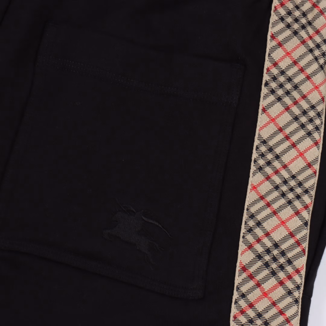 Burberry BBR Knight Side Plaid ShortsSingle-sided fish scale fabric woven with cotton as the base, the front is a smooth knitted surface, and the skin-touch surface is formed into a three-dimensional terry loop through the floating thread knitting technology of the knitting machine, which increases the fluffiness and delicate touch. The terry loop structure absorbs a large amount of water and evaporates quickly, and it is not easy to loosen and deform after multiple washings. The single-color flat embroidery on the back patch pocket body is controlled by the high-precision calculation system of the computer embroidery machine to control the coordinated operation of the machine head, needle bar, and bobbin. The fabric frame moves accurately in the horizontal and vertical directions to form a stitch track, adjust the tension of the upper and lower threads, ensure that the stitches are flat and free of floating threads, and form a fine pattern with an error of ±0.1mm. The fabric is evenly humidified by steam, squeezed with a heated roller and an elastic rubber blanket to force the fibers to shrink, and finally fixed by cooling with cold air. After treatment, the shrinkage rate is controlled within 3%, and the drawstring head is customized one to one