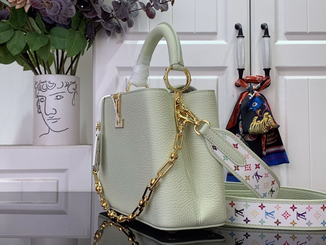 Crafted with playful proportions, the Capucines bag makes a modern statement with a fresh green hue of Taurillon leather, inspired by the rainbow palette of Japanese artist Takashi Murakami. The LV initials, lining, key bell and strap are accented with a joyful and colorful version of the House Monogram pattern, while gleaming gold hardware, including a detachable chain, completes the look with a polished touch.