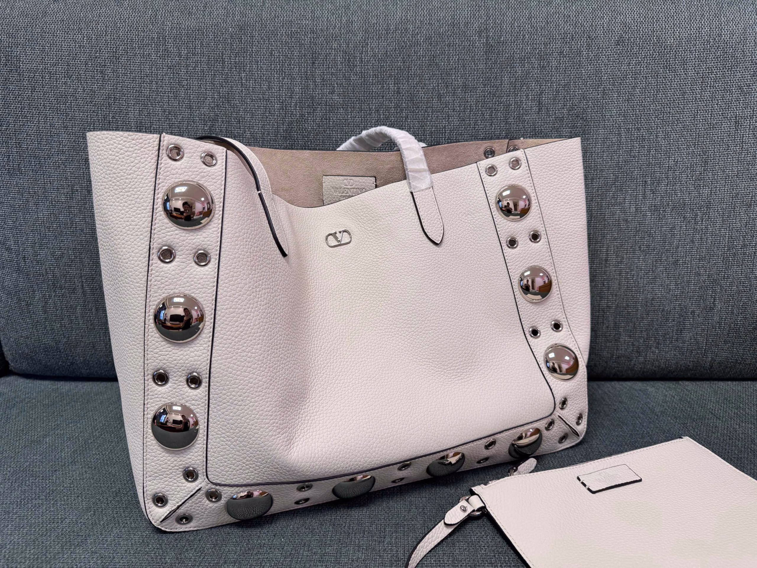 VALENTINO 🍃 GARAVANI NELLCOTEMedium-sized tote bag, decorated with spherical rivets and circular hollowed-out decorations. This bag can be carried by hand or comfortably on the shoulder through the handle.Palladium-plated metal accessories