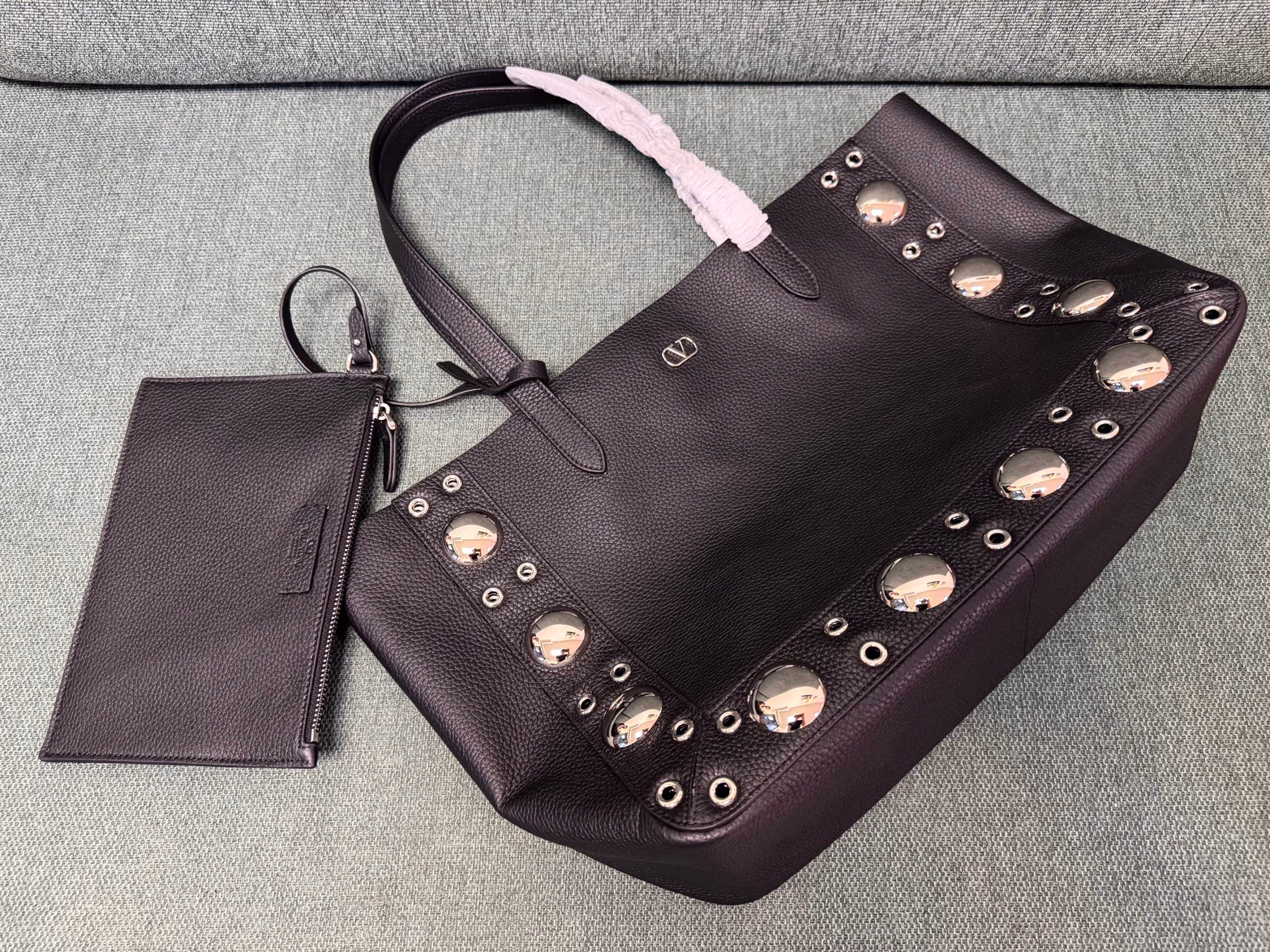 VALENTINO 🍃 GARAVANI NELLCOTEMedium-sized tote bag, decorated with spherical rivets and circular hollowed-out decorations. This bag can be carried by hand or comfortably on the shoulder through the handle.Palladium-plated metal accessories