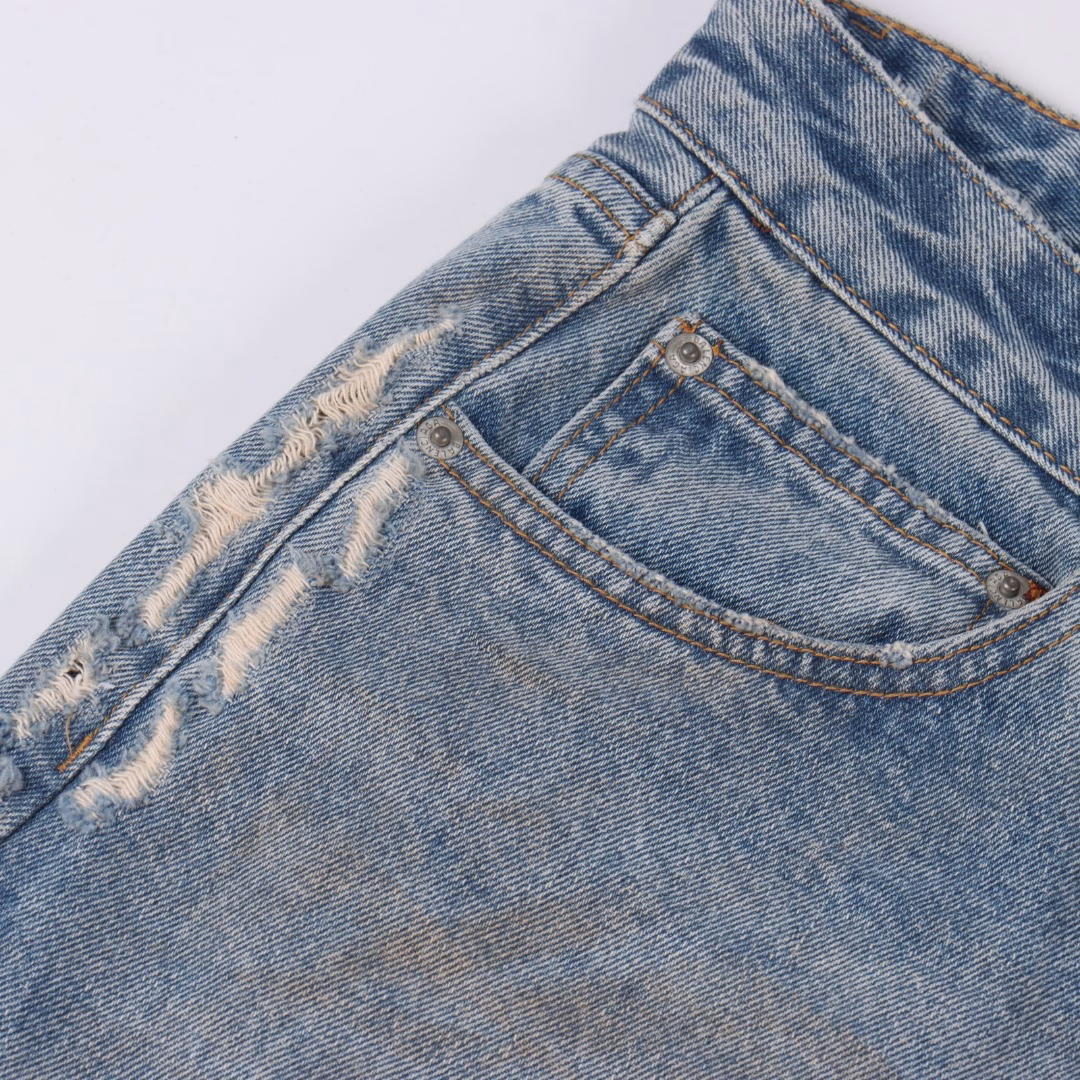 Balenciaga 25ss BAGGA wide-leg denim trousersIt is made of high-density cotton denim fabric and processed through a special blending technique, incorporating a trace amount of elastic fibers to enhance wearing comfort. The fabric undergoes multiple stages of water washing treatment, including enzyme washing, stone grinding and hand brushing, to create a natural fading effect and present a retro and aged texture. The yarn is spun by ring spinning technology to enhance the fabric's toughness and texture layering, ensuring a balance between stiffness and softness. Based on the classic straight-leg style, the leg lines are optimized through precise three-dimensional cutting. The front and rear pieces are spliced with a slight taper, ensuring a drape while avoiding bulkiness. The waistband design of the trousers may incorporate hidden adjustment loops, balancing a good fit and minimalist aesthetics. The buttons are made of specially crafted alloy and have undergone an aged coating treatment, engraved with the brand's signature LOGO. The rivets and zippers are made of the same series of metals and have passed salt spray tests to ensure oxidation resistance. At the same time, they maintain a rough industrial style, echoing the overall retro tone. Through the integration of deconstructionism and street style, the craftsmanship details are transformed into visual language - such as deliberately retained unfinished rough edges and asymmetrical dyeing, etc., strengthening the brand's rebellious spirit while maintaining the practicality of high-end items