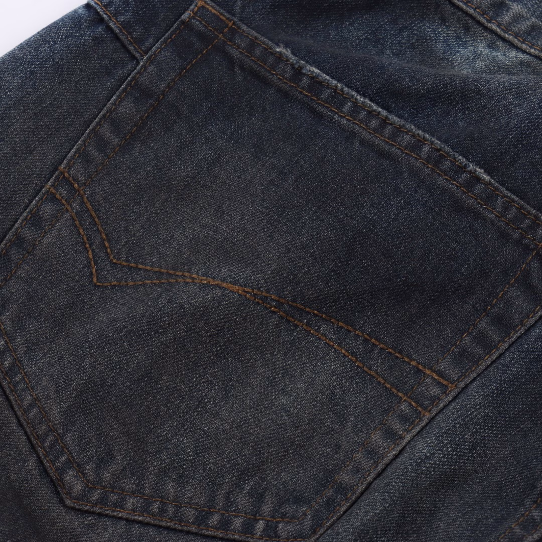Balenciaga 25ss show low-rise denim trousersIt is made of high-density cotton denim fabric and processed through a special blending technique, incorporating a trace amount of elastic fibers to enhance wearing comfort. The fabric undergoes multiple stages of water washing treatment, including enzyme washing, stone grinding and hand brushing, to create a natural fading effect and present a retro and aged texture. The yarn is spun by ring spinning technology to enhance the fabric's toughness and texture layering, ensuring a balance between stiffness and softness. Based on the classic straight-leg style, the leg line is optimized through precise three-dimensional cutting. The front and back pieces are slightly conical spliced to ensure a drape while avoiding bulkiness. The waistband design may incorporate hidden adjustment loops to balance fit and minimalist aesthetics. The buttons are made of specially designed alloy materials. The surface has undergone an aged coating treatment, engraved with the brand's signature LOG. The rivets and zippers are made of the same series of metals and have passed salt spray tests to ensure oxidation resistance. At the same time, it maintains a rough industrial style, echoing the overall retro tone. Through the integration of deconstructionism and street style, the craftsmanship details are transformed into visual language - such as deliberately retained unfinished burrs, asymmetrical dyeing, etc. Strengthen the brand's rebellious spirit while maintaining the practicality of high-end items