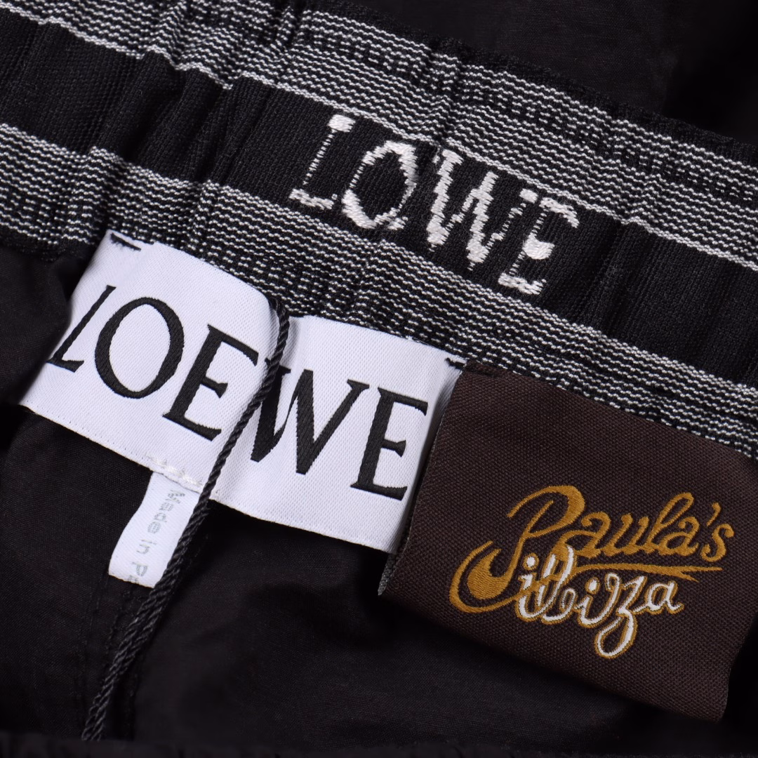 Loewe Back Pocket Hollow Embroidery ShortsMade of 32% nylon and 68% cotton blend. The hydrophobic fibers of nylon form microchannels to accelerate moisture discharge, with a moisture permeability of 4500g/m² for 24 hours, and the tear strength of nylon fibers reaches 45N, making the fabric have good wear resistance. The CAD plate making system is used to preset the solid embroidery area and the hollow area, and a high-precision Anagram embroidery of 35 needles/cm² is formed through a multi-head embroidery machine with a needle speed of 1000rpm. Then use the laser cutting process to accurately remove the base fabric in the embroidery hollow area to form a geometric hole shape. The laser accuracy of ±0.1mm makes the hollow part smooth and without burrs. The overall line is straight and delicate, the fabric is comfortable and soft, and the color is consistent without color difference. It can be matched with the same style to create a fashionable look, suitable for various occasions, customized accessories, three standards are complete, and the same style for men and women
